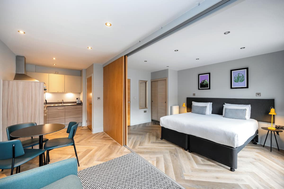 A modern hotel room with a large bed, a desk, and a dining area.