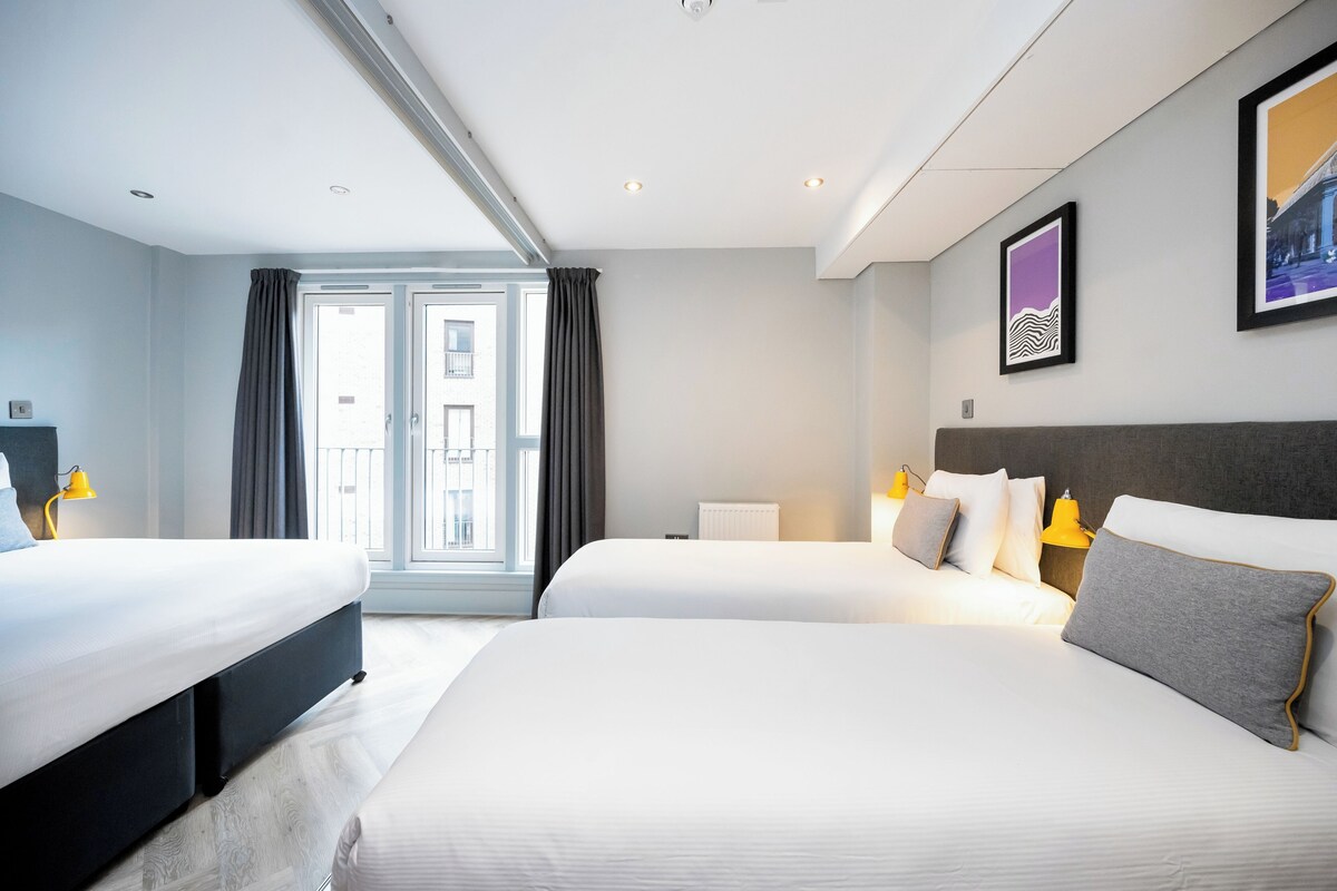 A hotel room with two beds, a large window, and a view of the city.