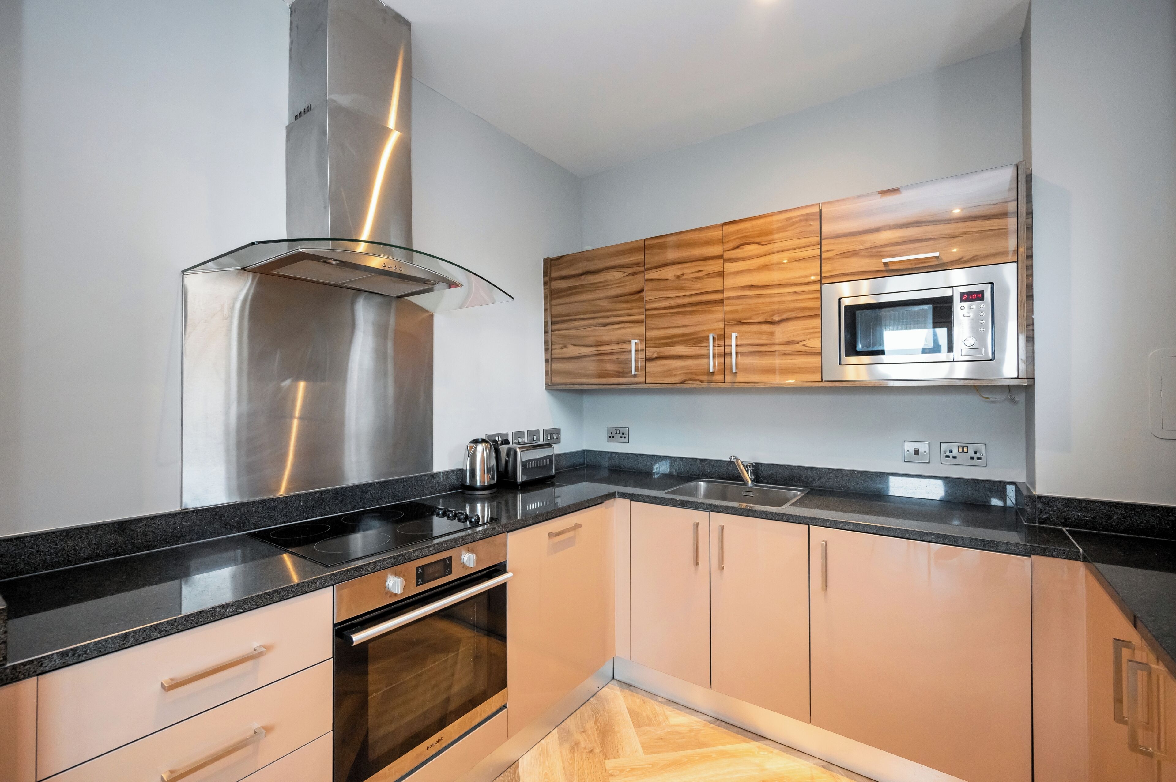 A modern kitchen with a stainless steel range hood, a built-in microwave, and wooden cabinets.
