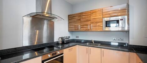 A modern kitchen with a stainless steel range hood, a built-in microwave, and wooden cabinets.