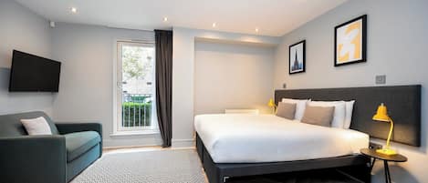 A modern bedroom with a bed, a sofa, a TV, and a window with curtains.