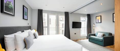 A modern hotel room with a large bed, a sofa, a TV, and a view of the city through the window.