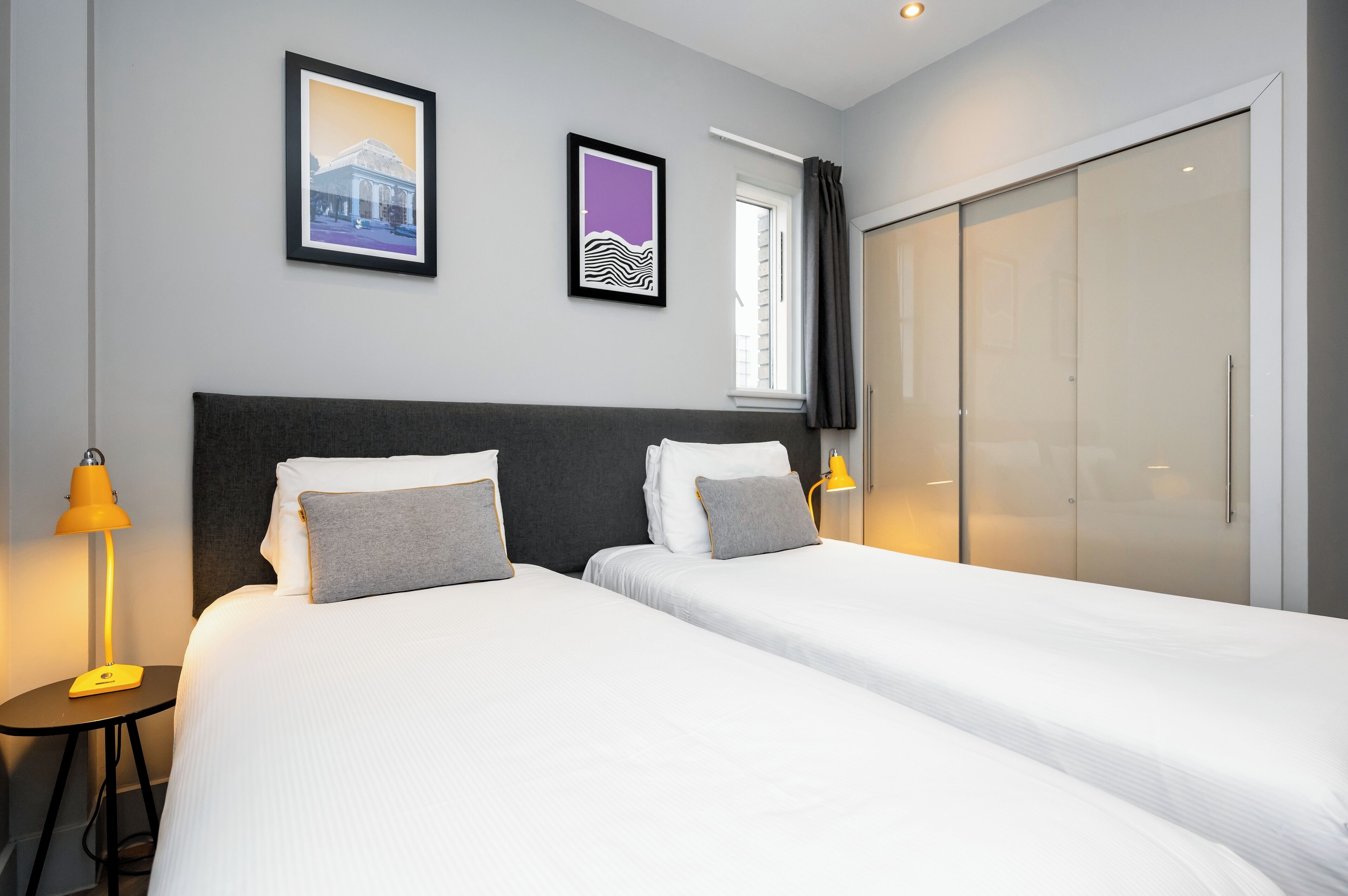 A hotel room with two beds, a large wardrobe, and two framed pictures on the wall.
