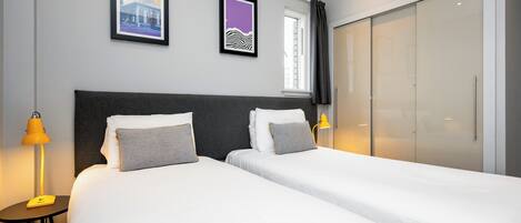 Une chambre d’hôtel avec deux lits, une grande armoire et deux tableaux encadrés au mur.