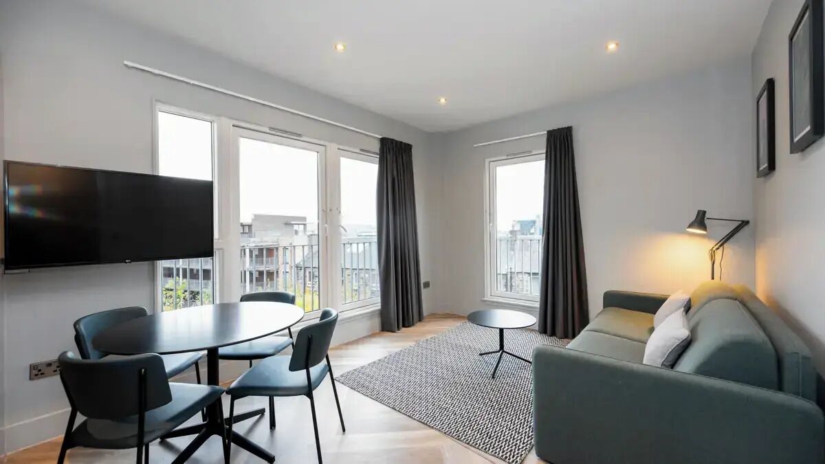 Een moderne woonkamer met een flatscreen televisie, een ronde eettafel met stoelen, een bank en een klein bijzettafeltje.