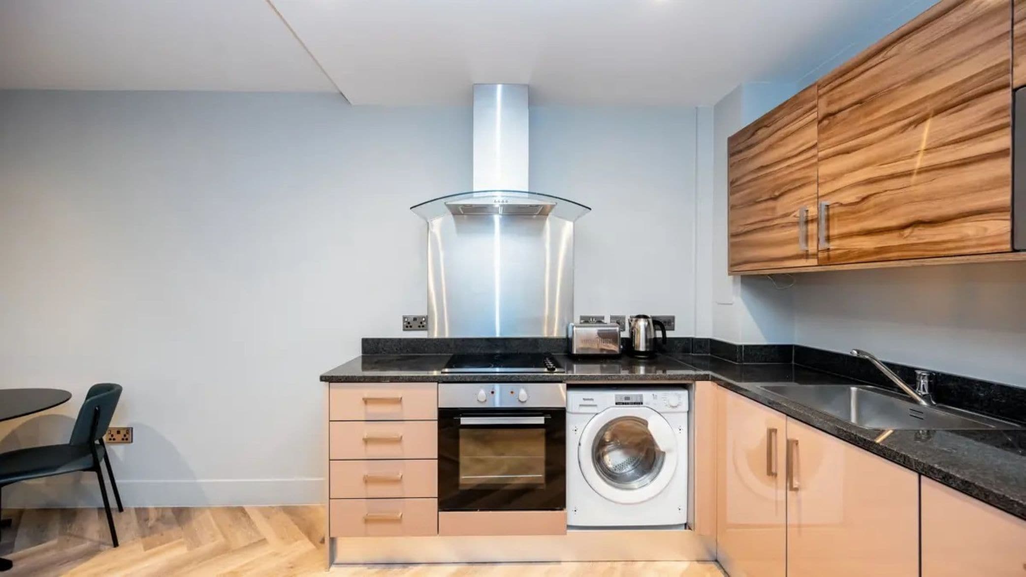 A compact kitchen with a built-in oven, a washing machine, and wooden cabinets.