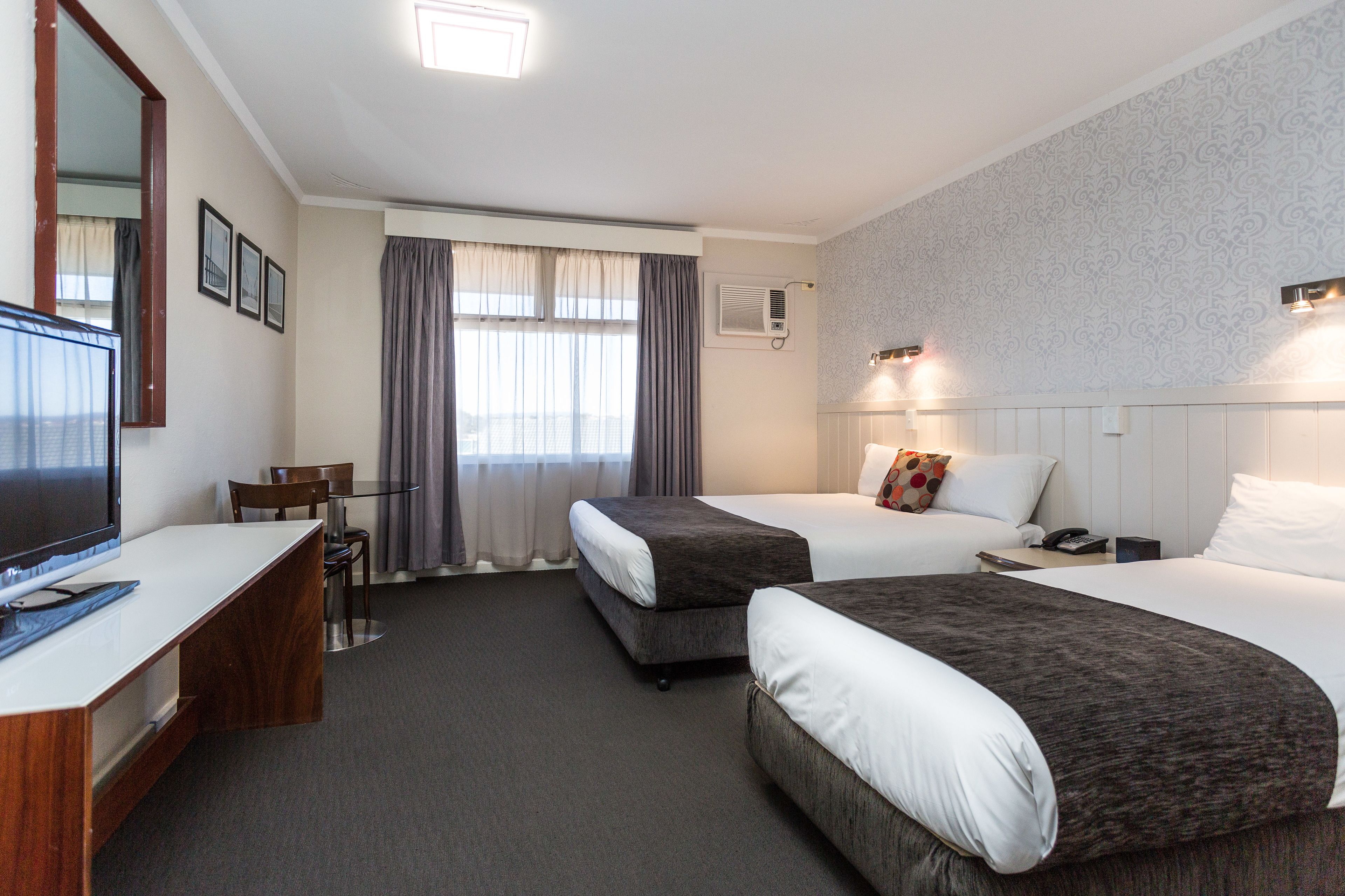 A hotel room with two beds, a desk, a TV, and a window with curtains.