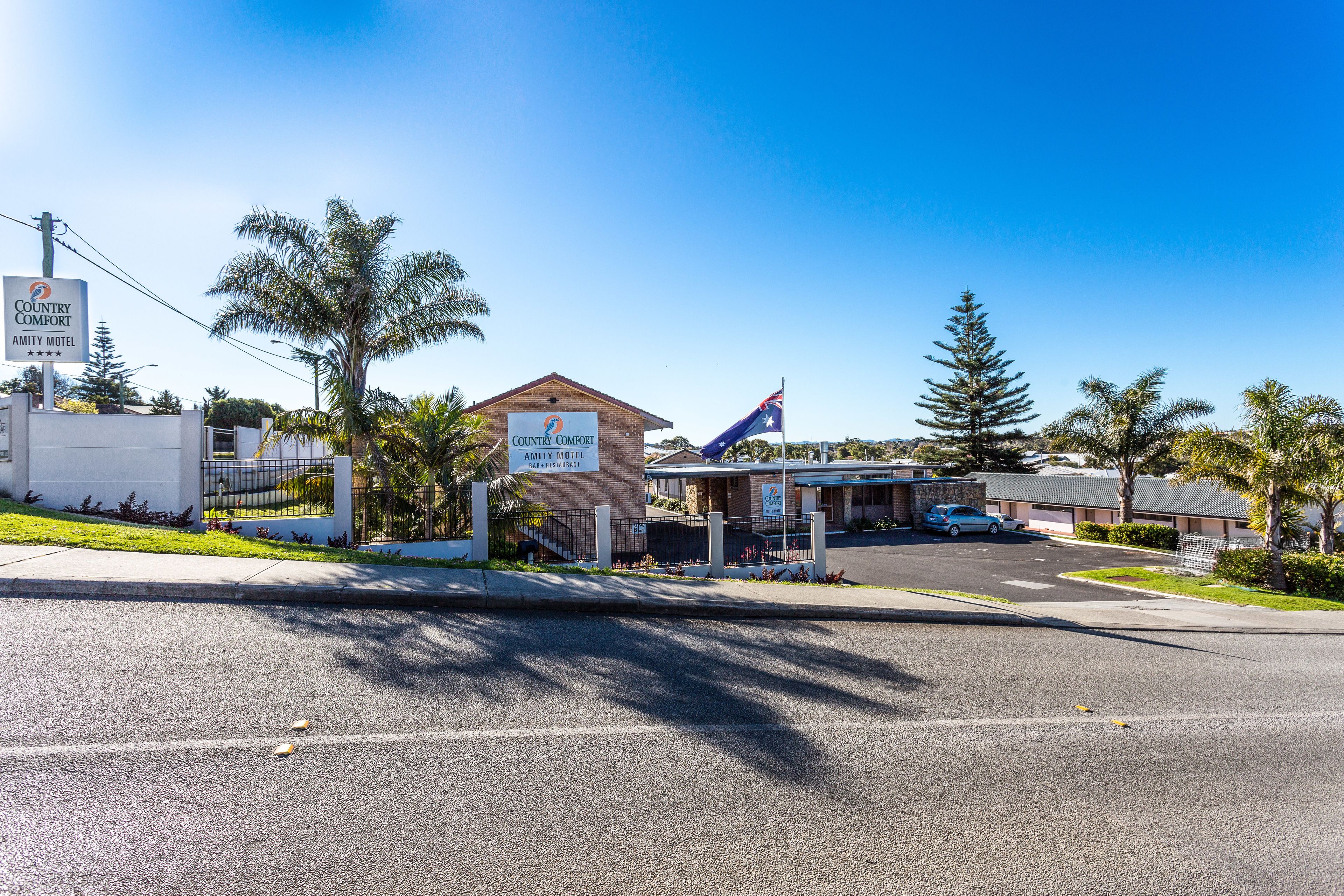 A Country Comfort Amity Motel with a flag, palm trees, and a clear blue sky.