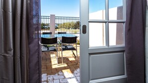 Una porta aperta che dà su un patio con tavolo e sedie, una recinzione in metallo e un cielo azzurro limpido.