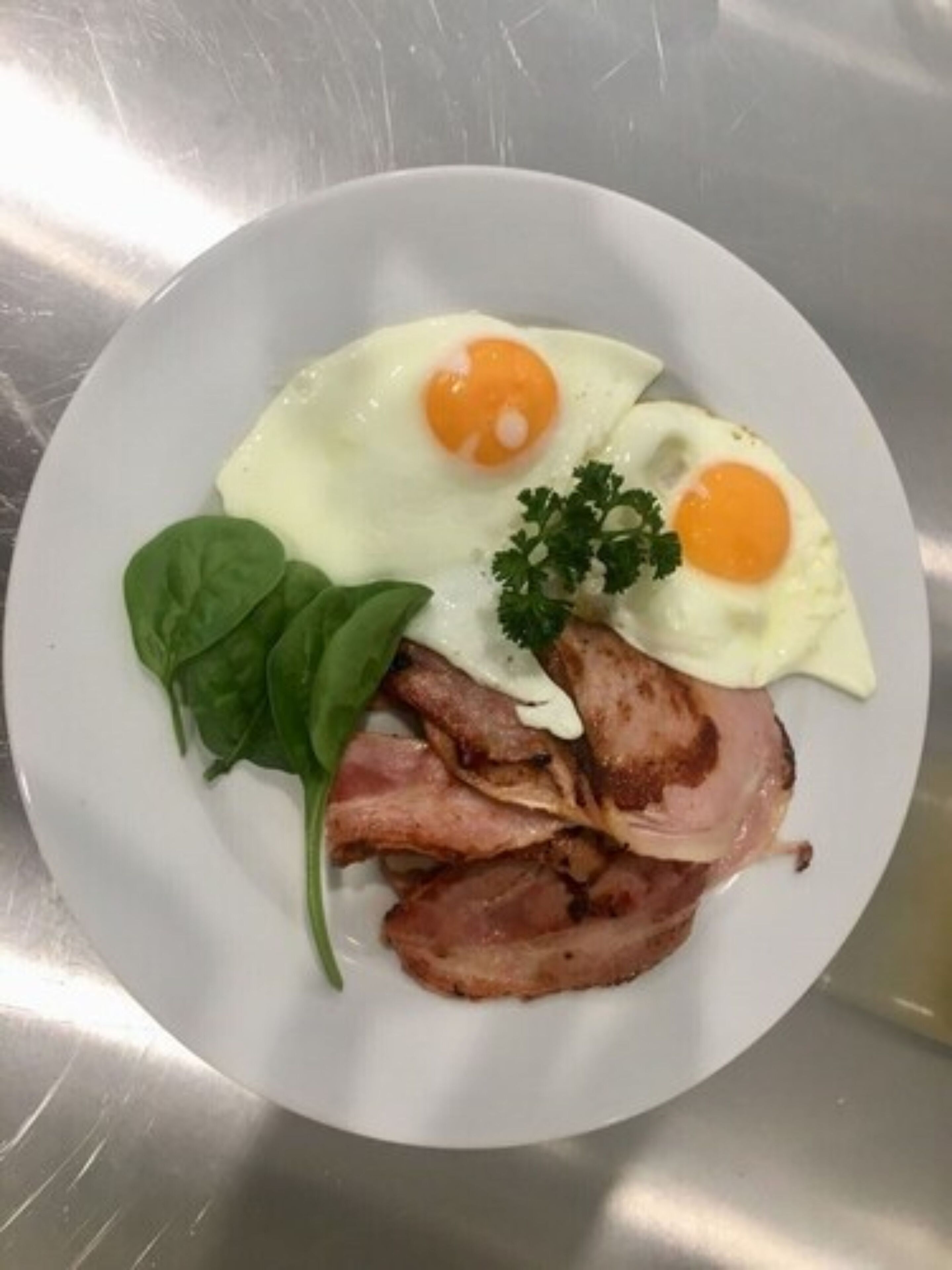 A plate with two fried eggs, slices of bacon, and a sprig of parsley.
