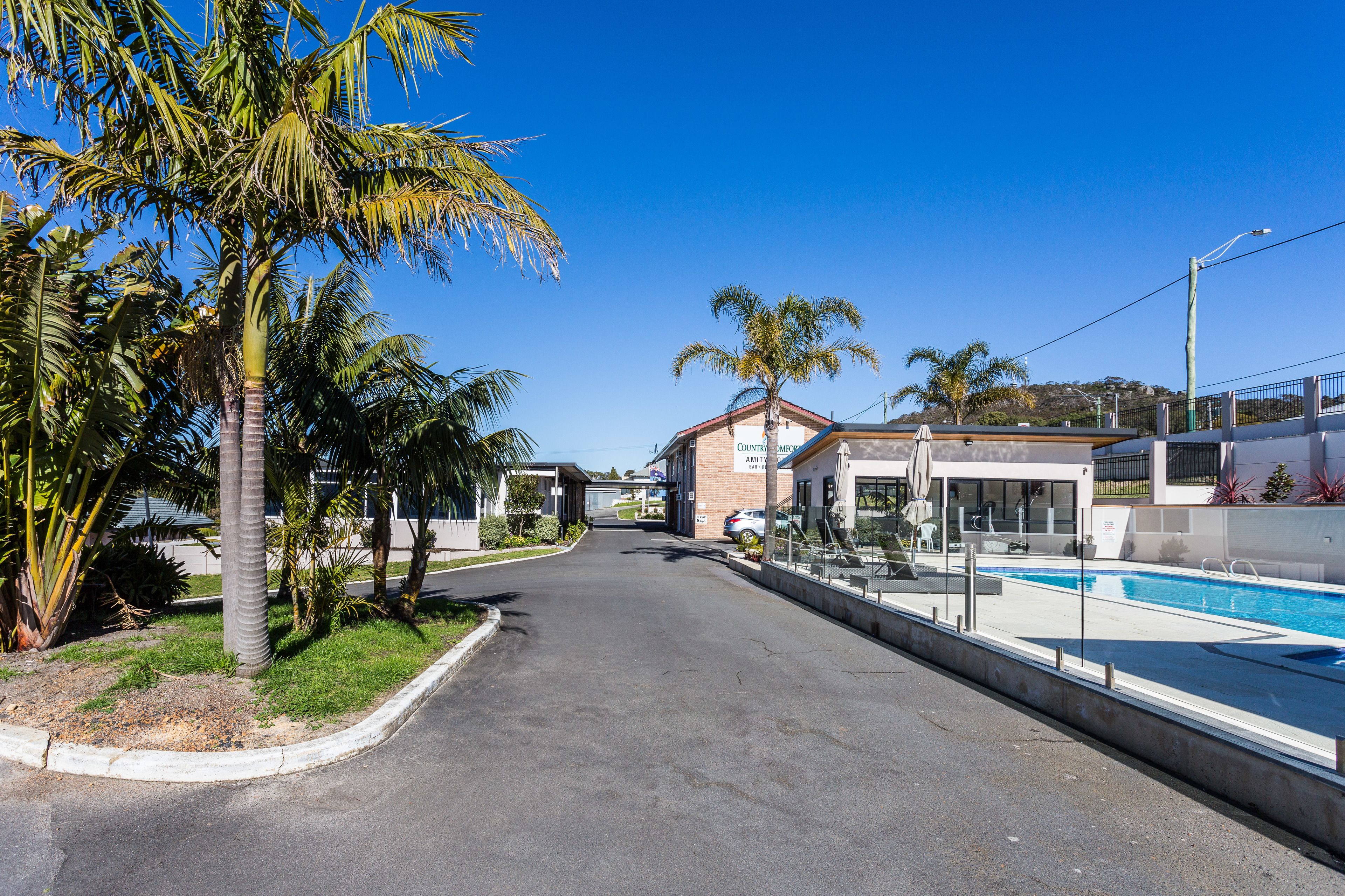 Una calle con piscina, palmeras y un edificio con un cartel que dice "COSTA RIVER".