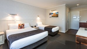 Camera d'albergo con due letti, una piccola scrivania, un frigorifero e un quadro appeso al muro.