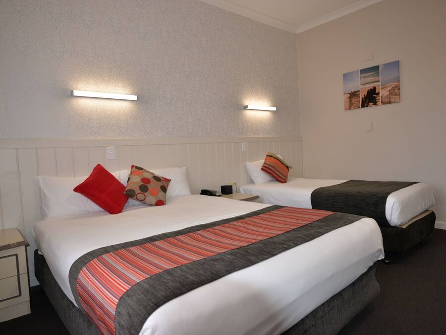 Ein Hotelzimmer mit zwei Betten, jeweils mit Kissen und Decke. Ein Nachttisch mit Lampe und Telefon steht bereit. Die Wände sind mit einem gemusterten Wandpapier versehen und es hängt ein Gemälde an der Wand.