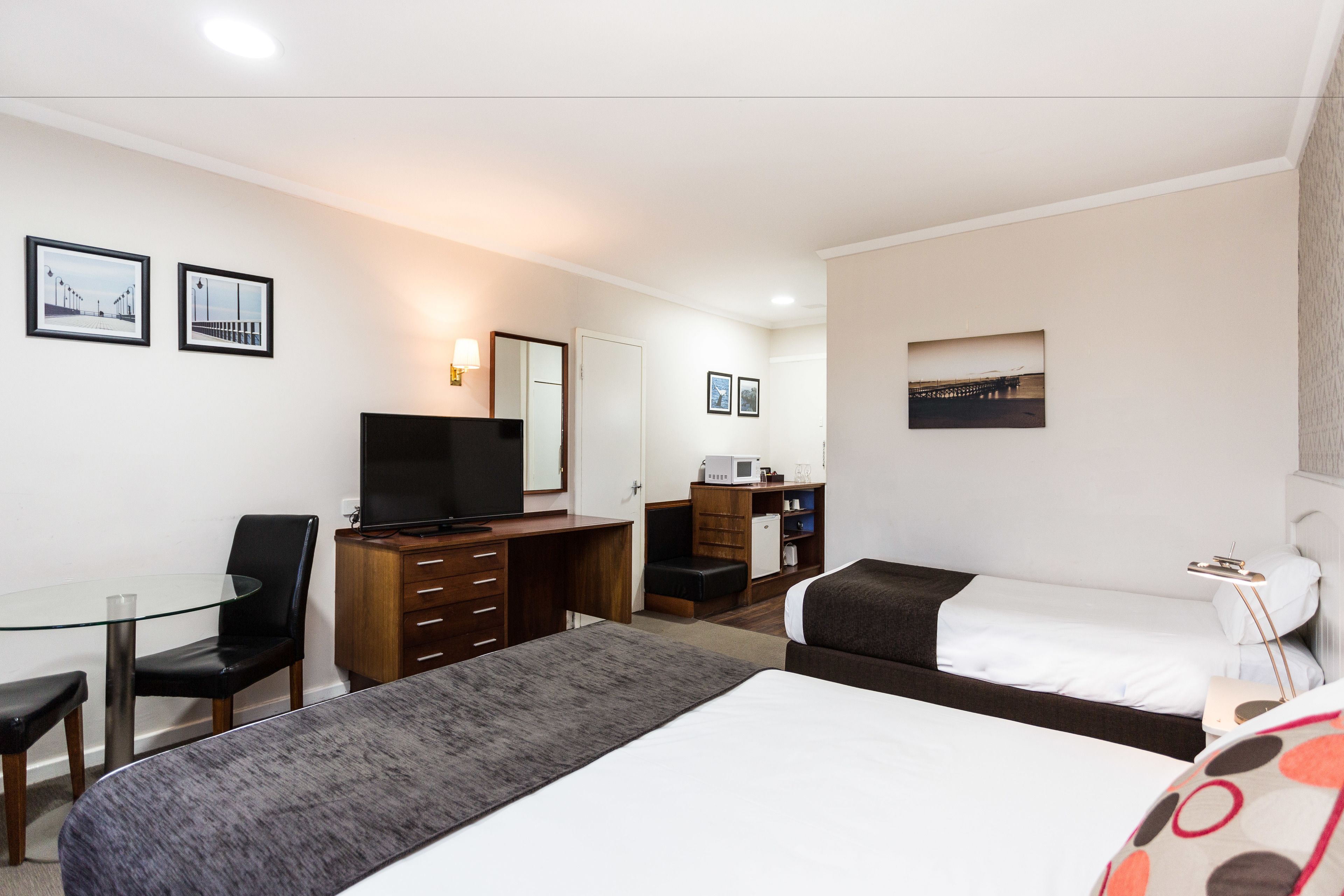 A hotel room with a bed, a desk with a TV, a chair, a small kitchenette, and a window with a view.