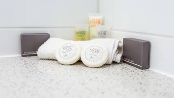 Ein Badezimmer mit weiß gefliester Wand, einem Duschorganisator, zwei Gesichtsseifen, einem Haargel und einer Toilettenartikel-Tasche.