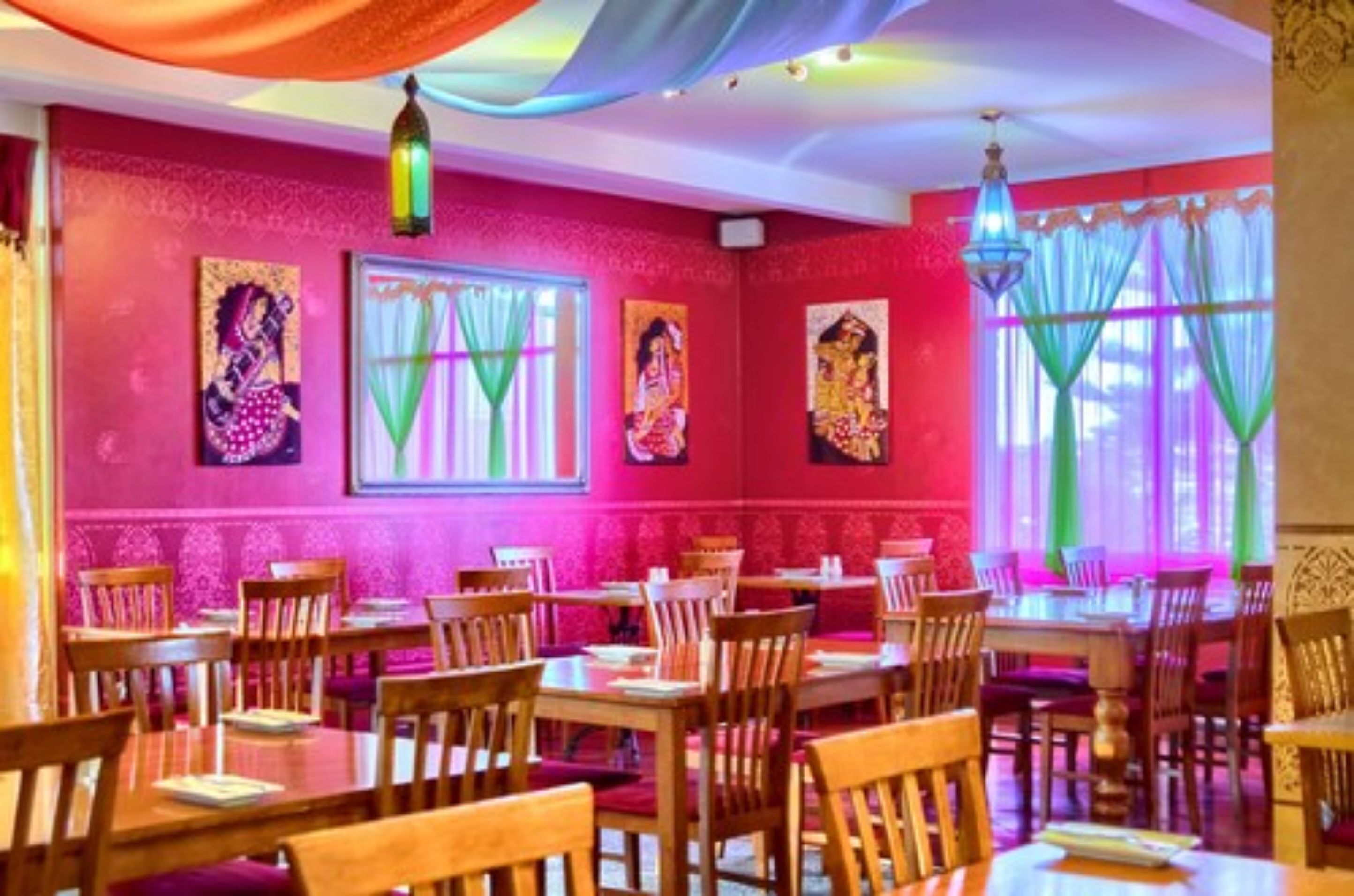 A restaurant with wooden tables and chairs, pink walls, and artwork.