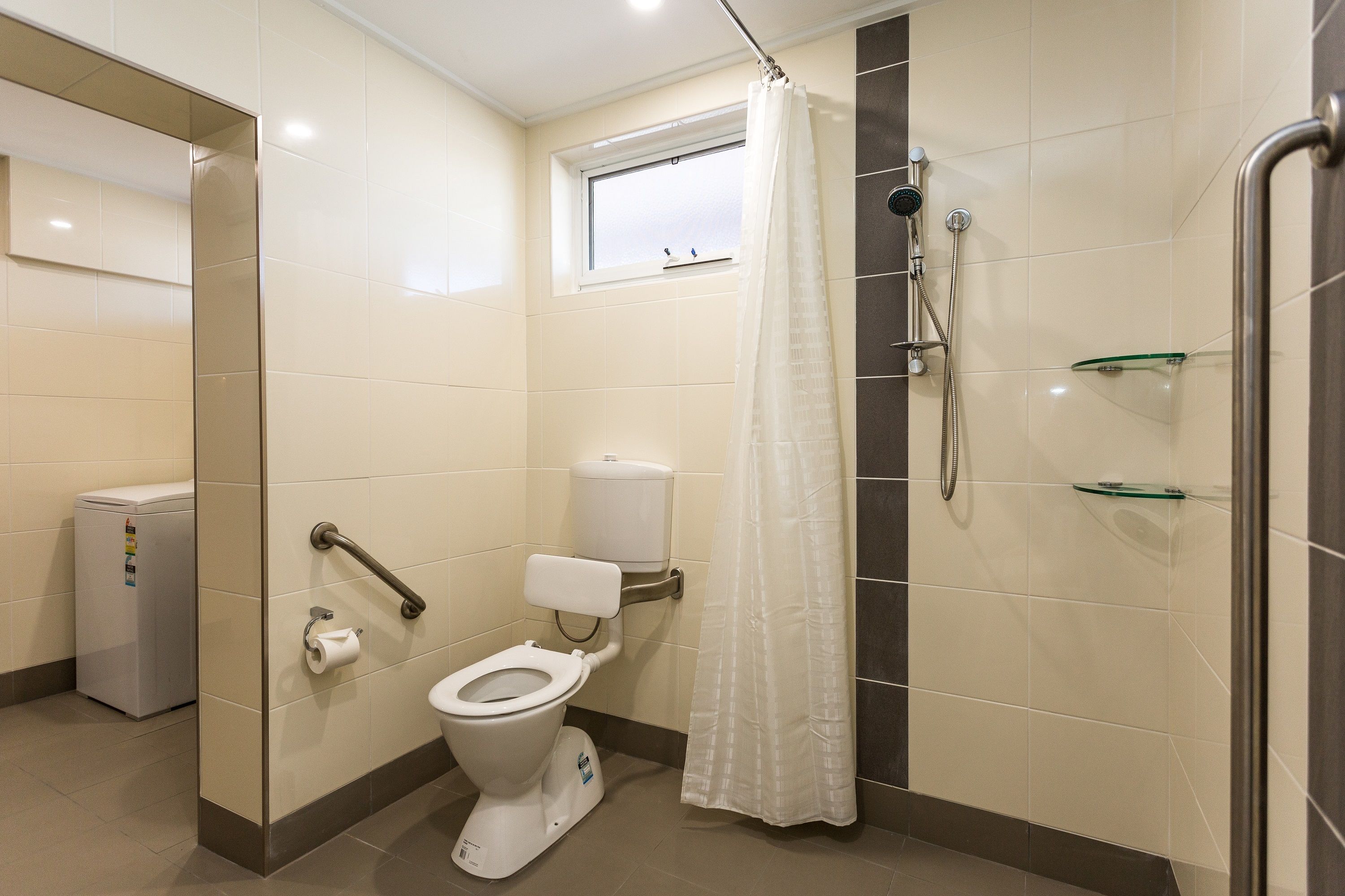 A modern bathroom with a toilet, shower, and a window above the toilet.