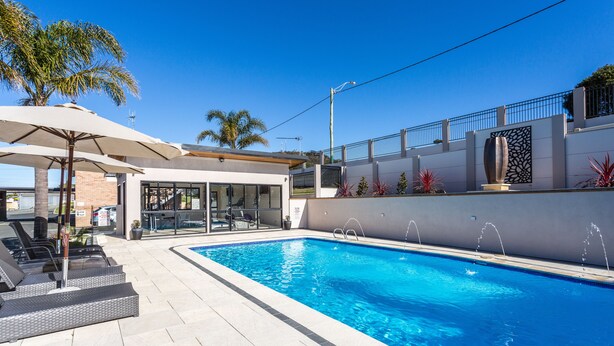 Una piscina con lettini e ombrelloni, un edificio moderno con porte in vetro e un cielo azzurro limpido.