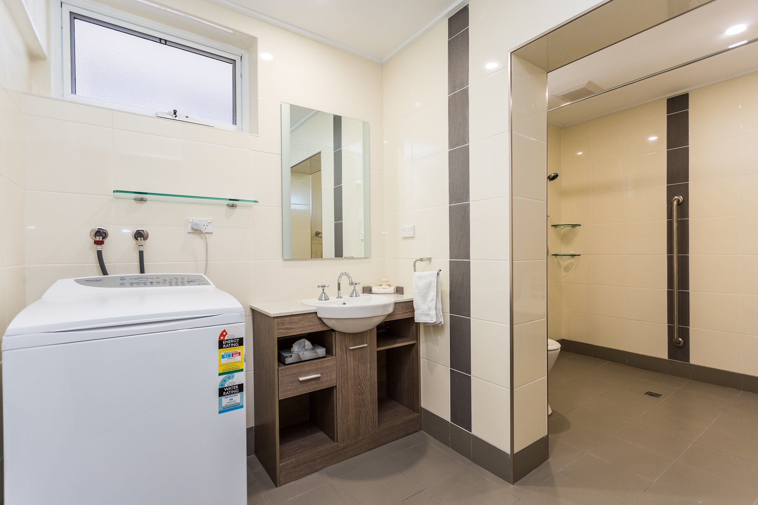 A modern bathroom with a built-in washing machine, a sink, and a glass shower enclosure.