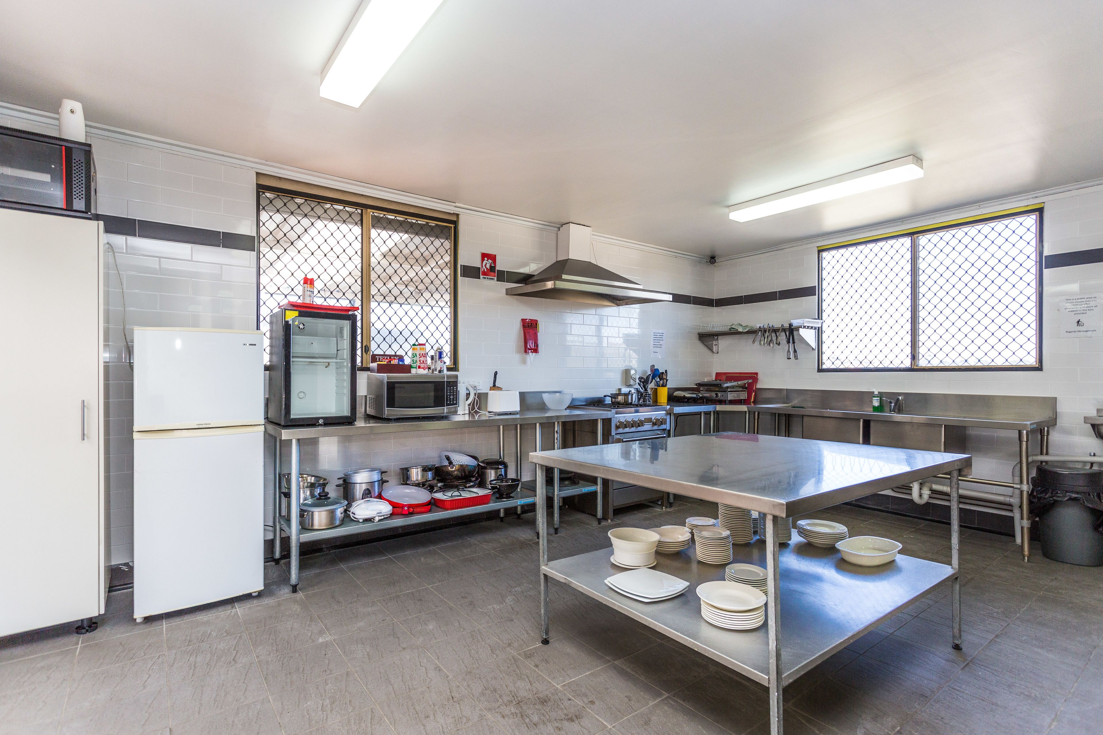 A commercial kitchen with stainless steel appliances, a large table with plates, and a tiled floor.
