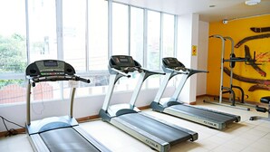 Three treadmills in a gym with large windows and a yellow wall. - MeStyle Place Hotel (Bangkok)