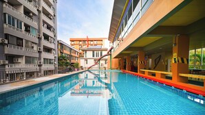 A swimming pool with a clear blue water surface, surrounded by multi-story buildings with balconies and air conditioning units. - MeStyle Place Hotel (Bangkok)