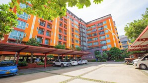 A multi-story hotel with a vibrant orange facade, a covered parking area, and several cars parked in front. - MeStyle Place Hotel (Bangkok)