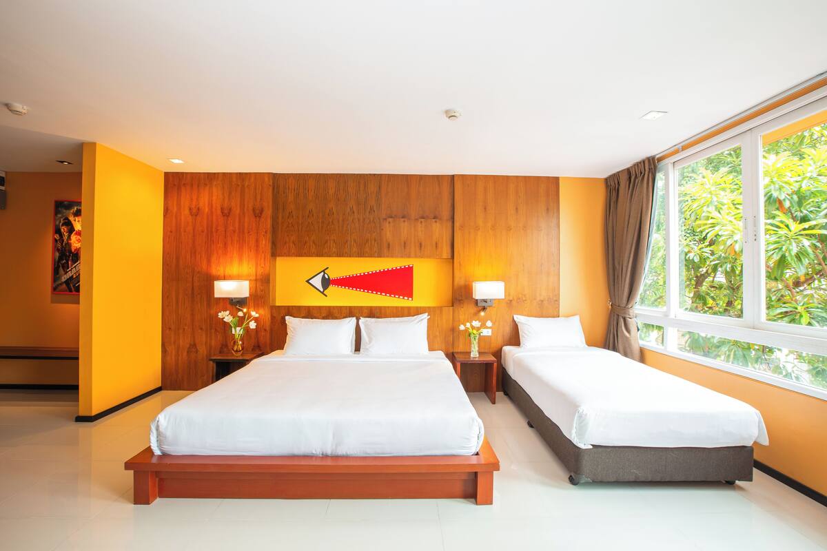 A hotel room with a large bed, two bedside tables, a wooden headboard, and a window with a view of greenery.