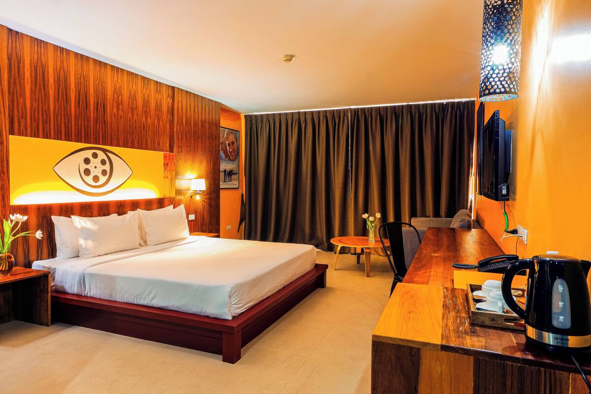 A hotel room with a large bed, a desk with a telephone and a coffee maker, a chair, and a curtain.
