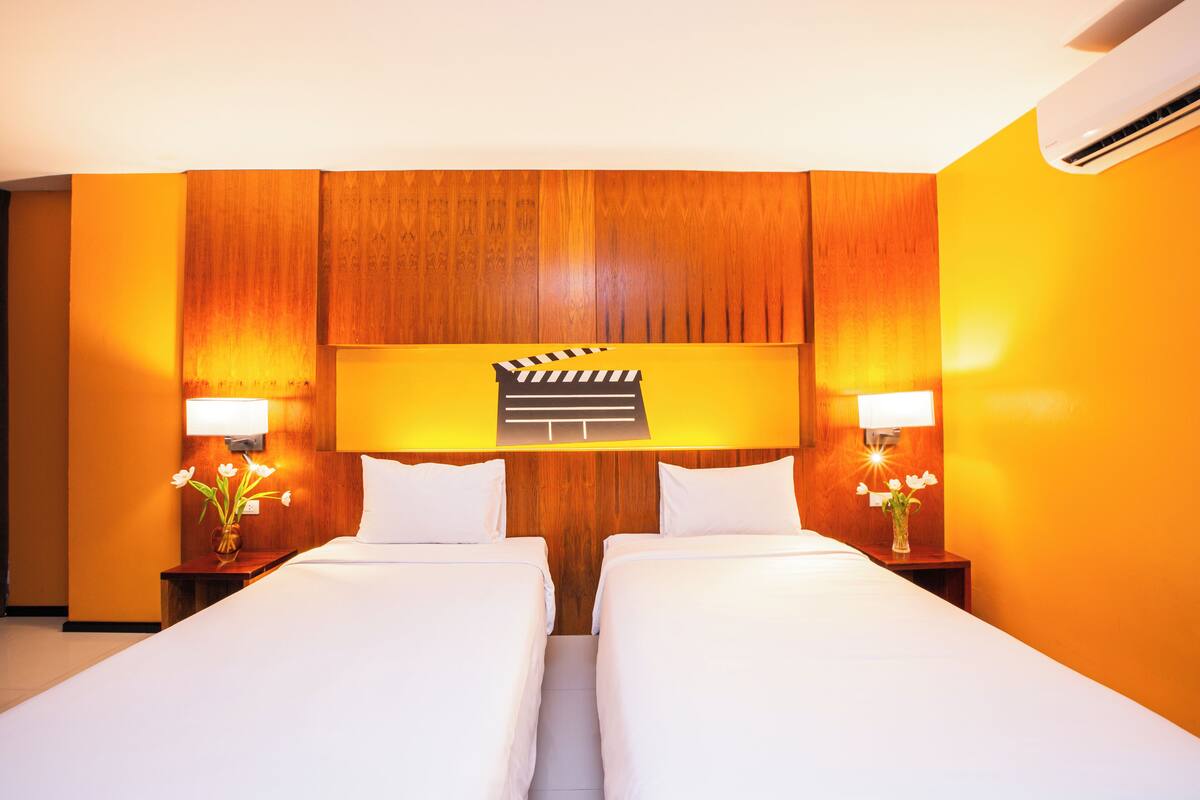 A hotel room with two beds, wooden headboard, bedside lamps, and a clapperboard decoration.