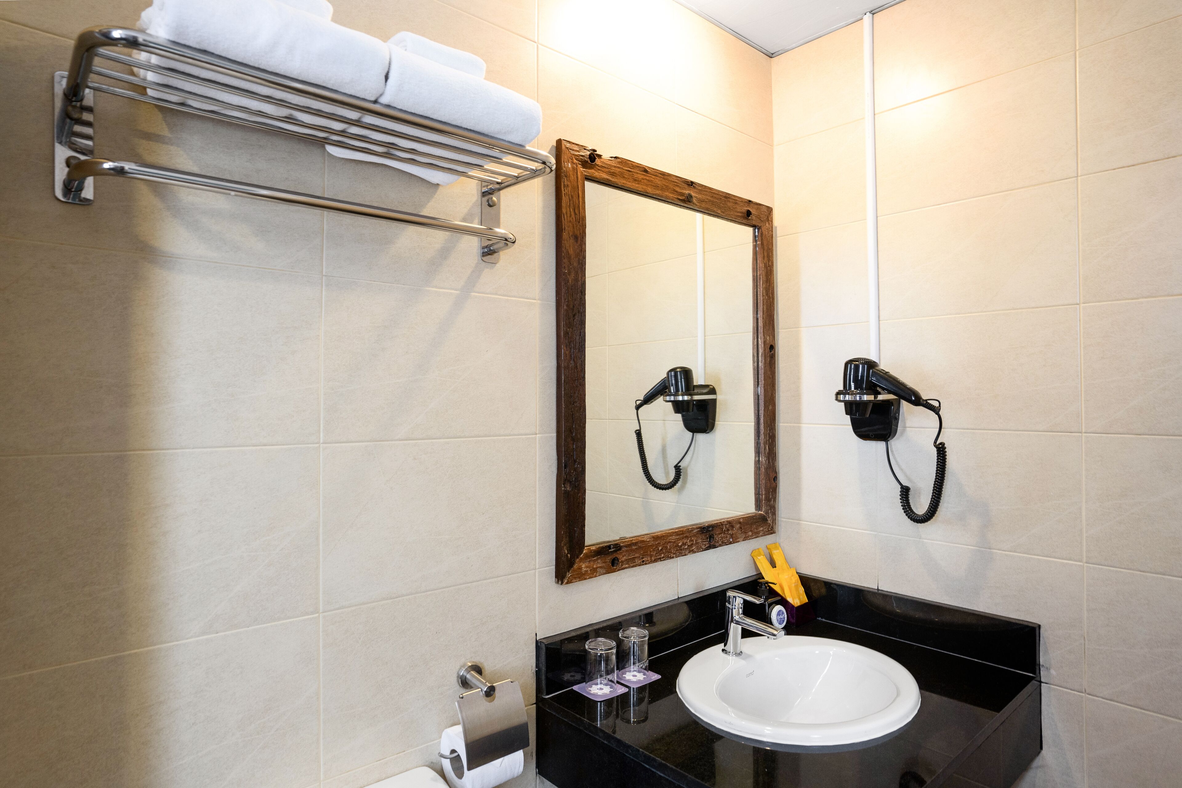 Een badkamer met een witte wastafel, een spiegel met houten lijst, een handdoekhouder met handdoeken en een haardroger aan de muur.