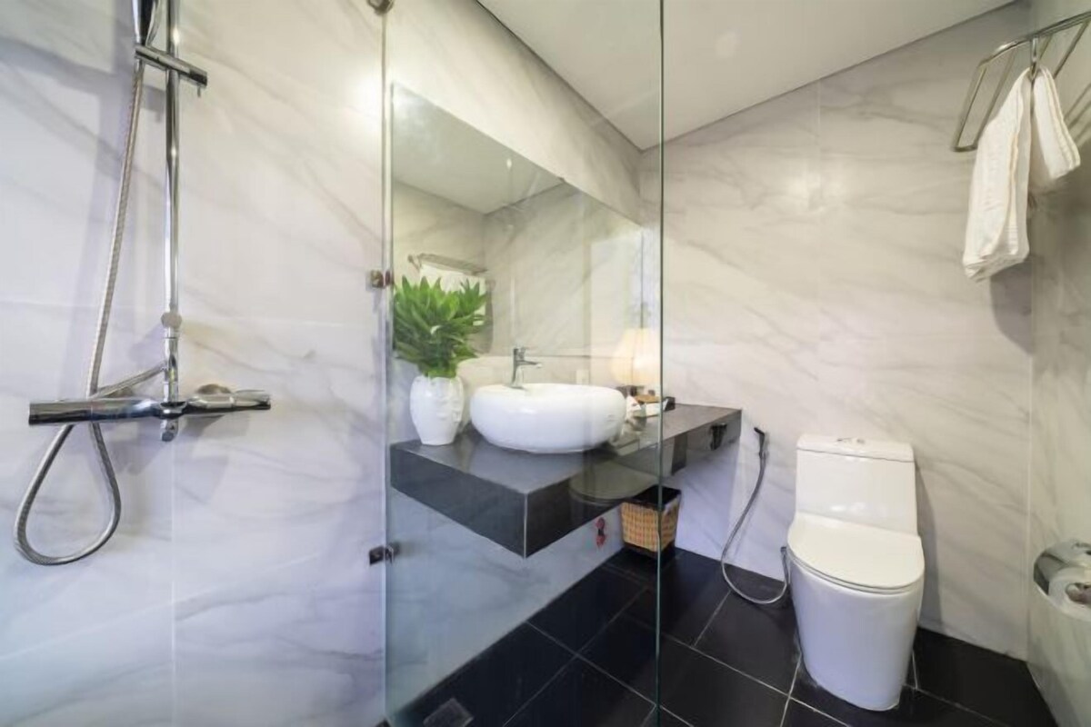 A modern bathroom with a glass shower enclosure, a white sink, a black countertop, and a white toilet.