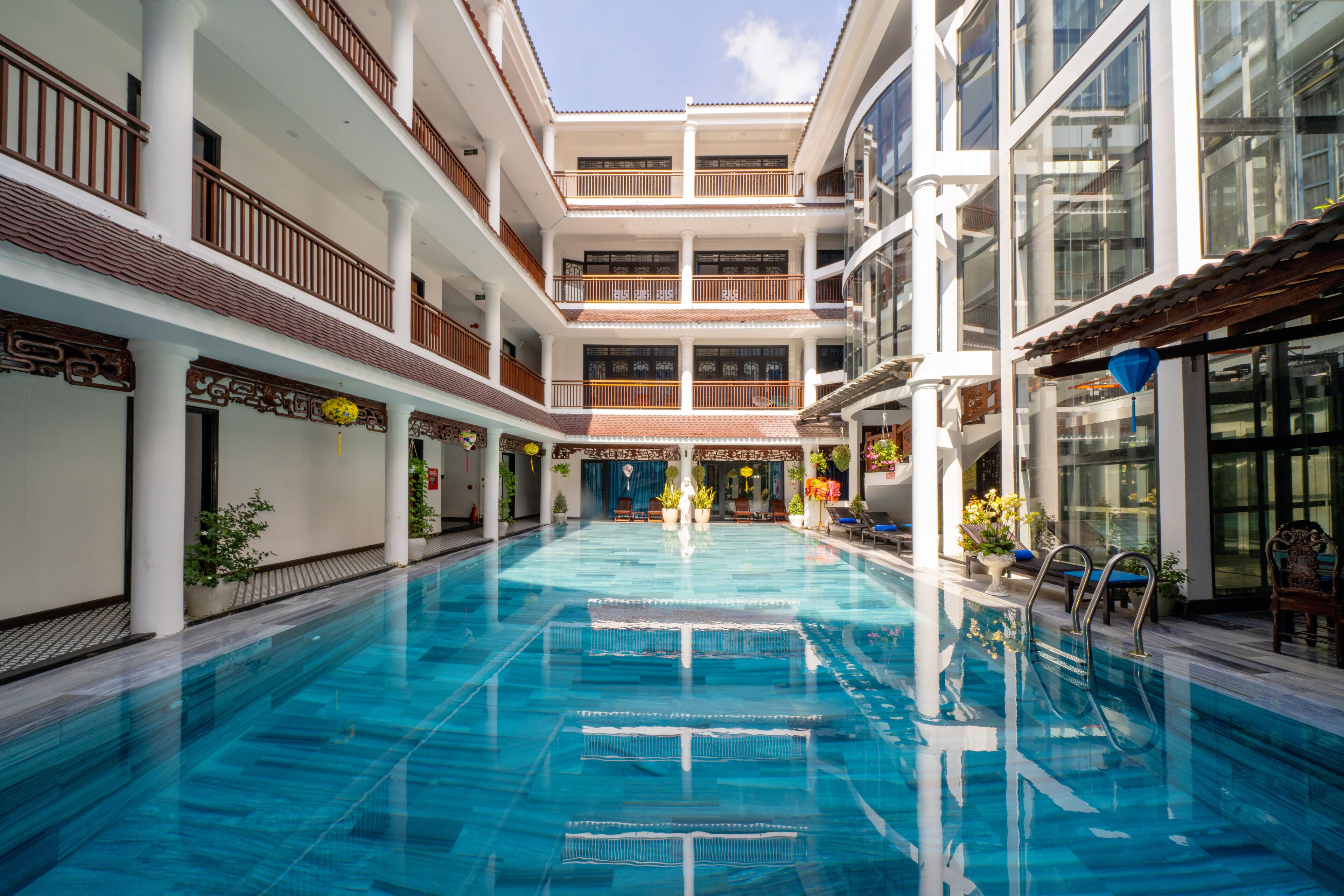 A multi-level indoor swimming pool with clear water, surrounded by balconies with wooden railings and potted plants.