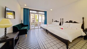 Habitación de hotel con dos camas, un escritorio con lámpara, un sofá verde y piso estampado.