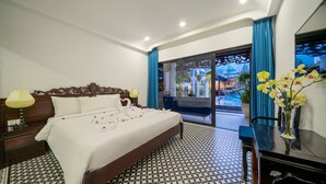 Habitación de hotel con una cama grande, un escritorio con un florero y vistas al exterior a través de un ventanal.