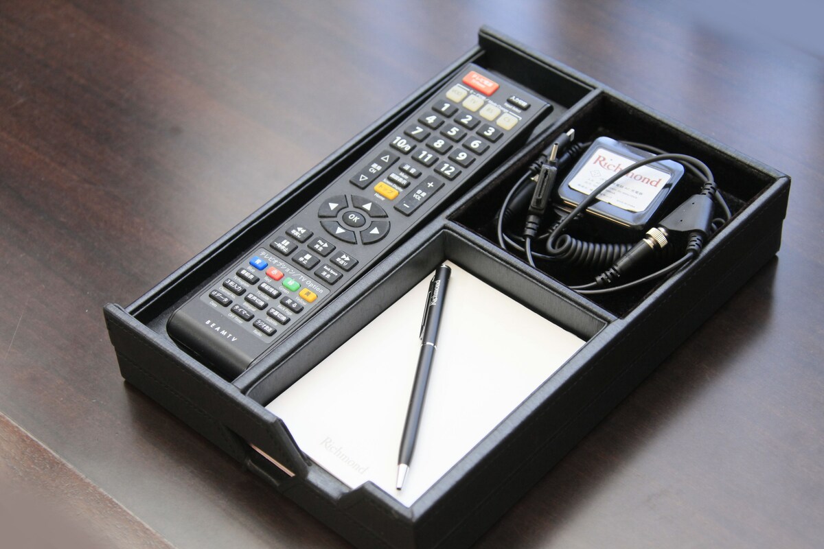 A black remote control, a pen, and a charger in a black box.