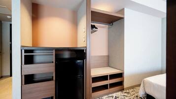 A compact hotel room with a kitchenette, built-in shelving, a bed, and a patterned rug.