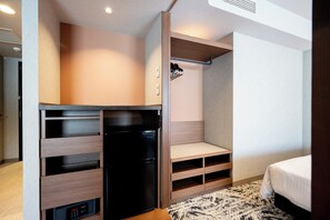 Habitación de hotel compacta con kitchenette, estanterías integradas, cama y alfombra estampada.