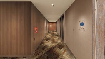 A hotel hallway with wooden paneling, a patterned carpet, and a red emergency exit sign.