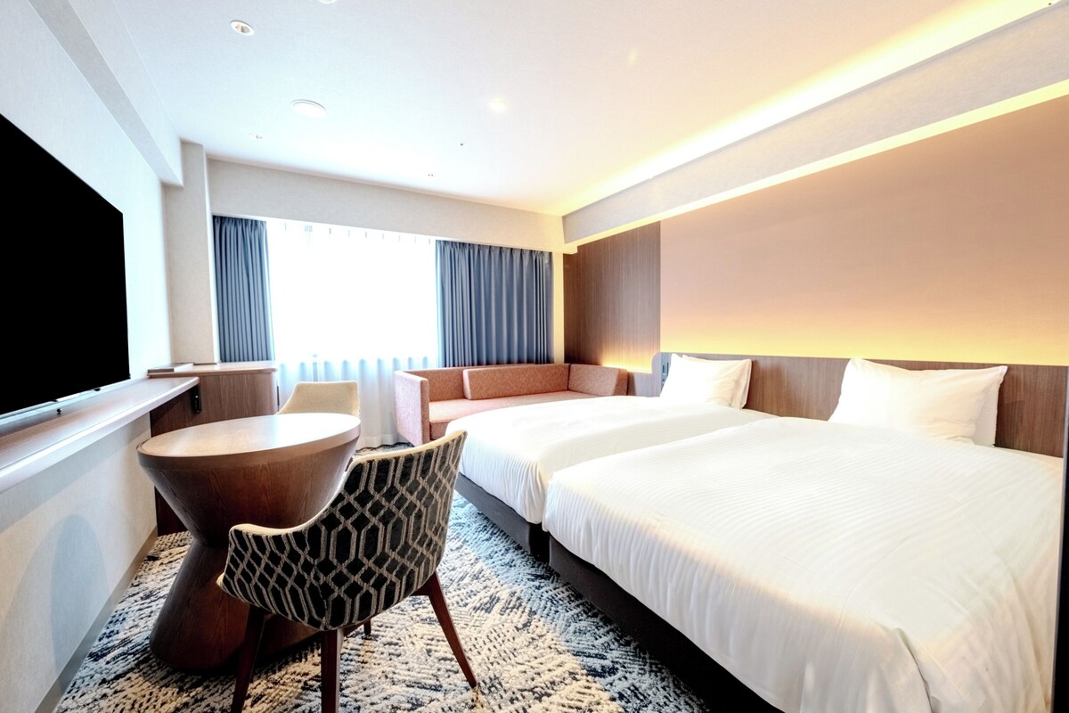 Una habitación de hotel con cama, sofá, televisión, mesa y silla.