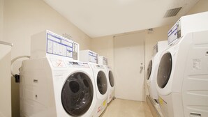 A row of white front-loading washing machines in a laundry room with beige walls and a tiled floor. - Richmond Hotel Fukuoka Tenjin (Fukuoka)
