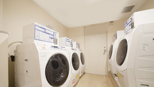 A row of white front-loading washing machines in a laundry room with beige walls and a tiled floor. - Richmond Hotel Fukuoka Tenjin (Fukuoka)
