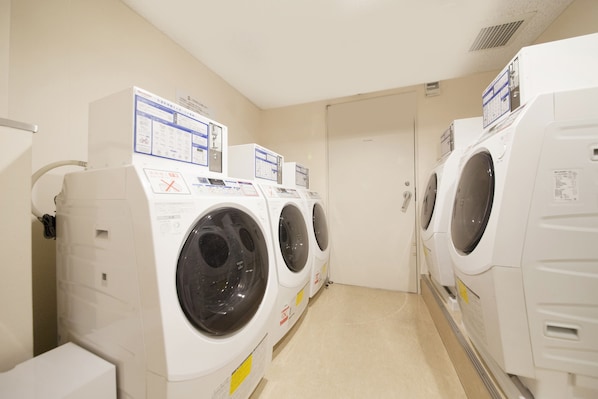 A row of white front-loading washing machines in a laundry room with beige walls and a tiled floor. - Richmond Hotel Fukuoka Tenjin (Fukuoka)