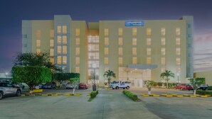 A modern hotel with a large entrance, multiple floors, and a parking area with cars and a van. - City Express by Marriott Minatitlan (Minatitlán)