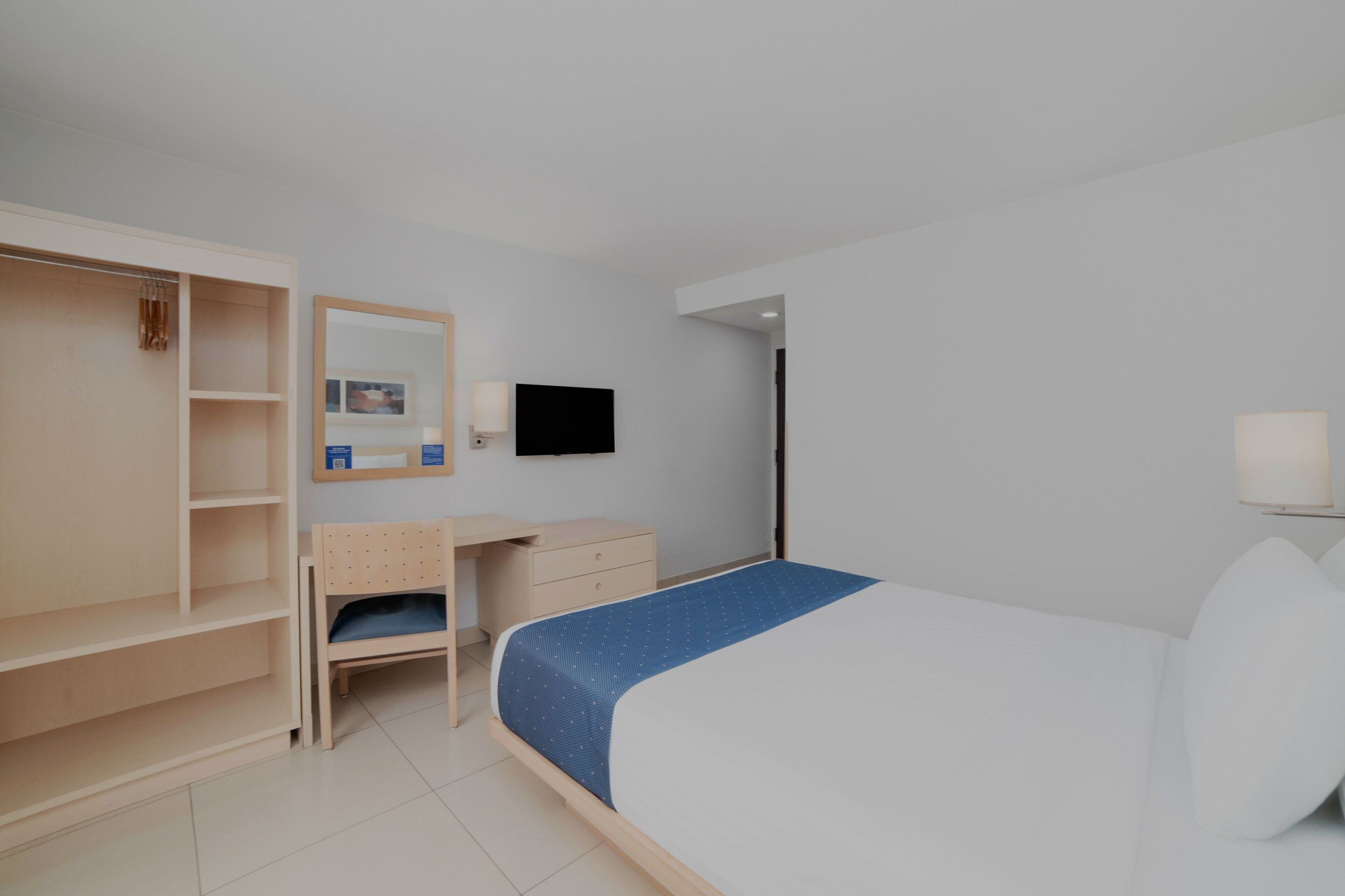 Una habitación de hotel con cama, escritorio, armario, televisor y espejo.