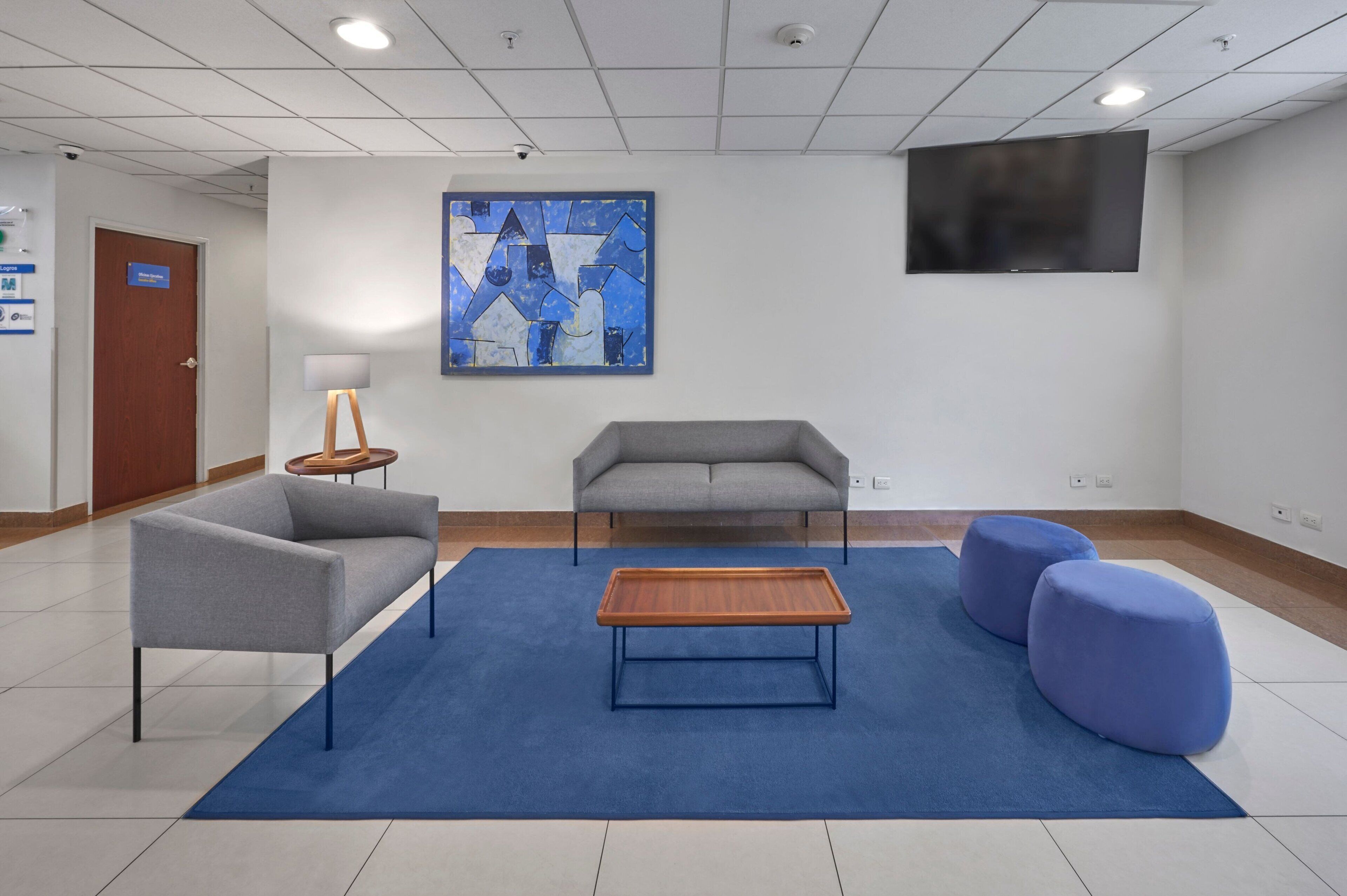 Un vestíbulo moderno con un sofá gris, una mesa de centro de madera y otomanas azules.