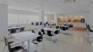 A spacious cafeteria with white tables and black chairs, large windows, and a counter area with food and beverages. - City Express by Marriott Minatitlan (Minatitlán)