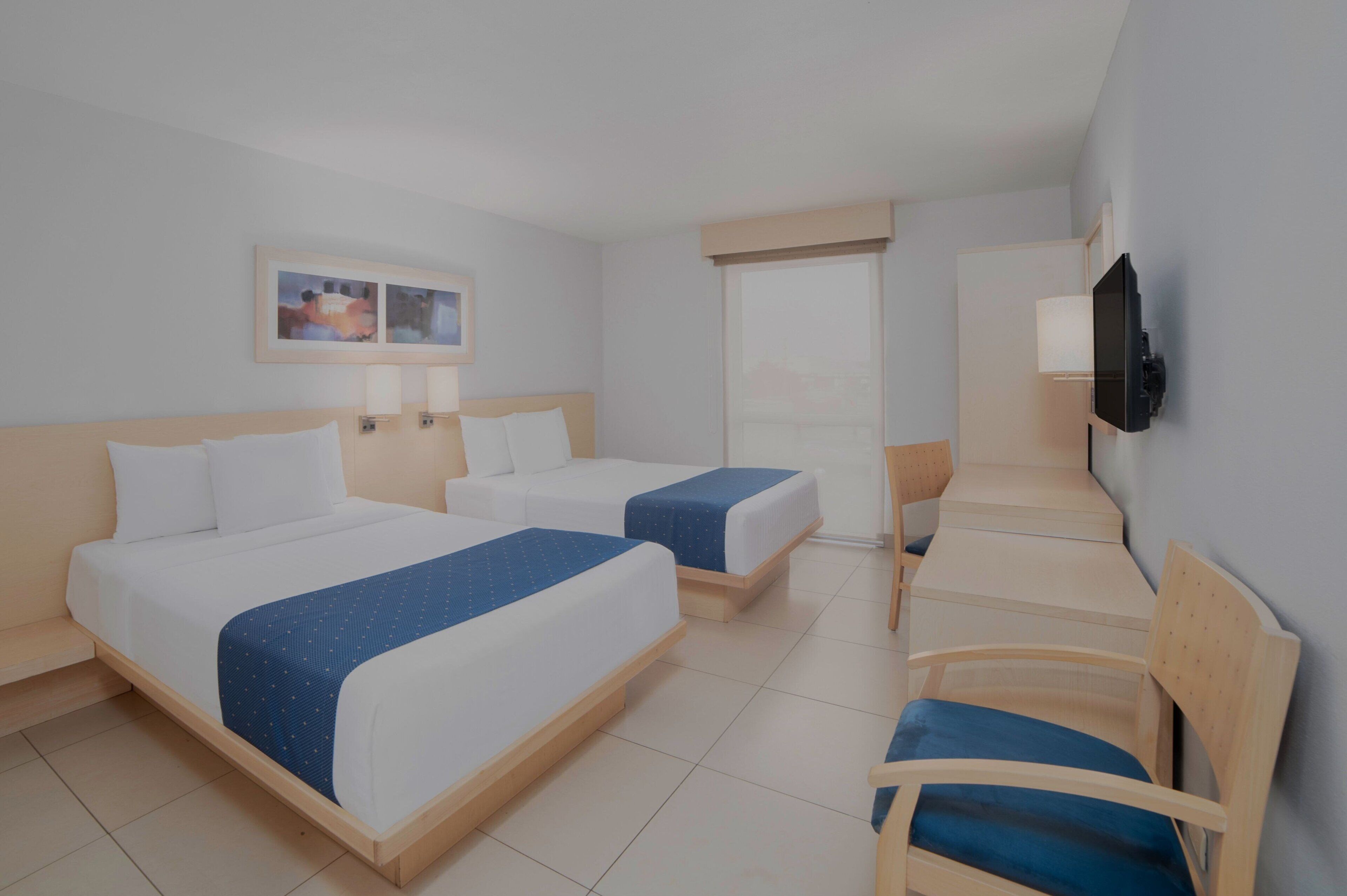 A hotel room with two beds, a TV mounted on the wall, and a chair.