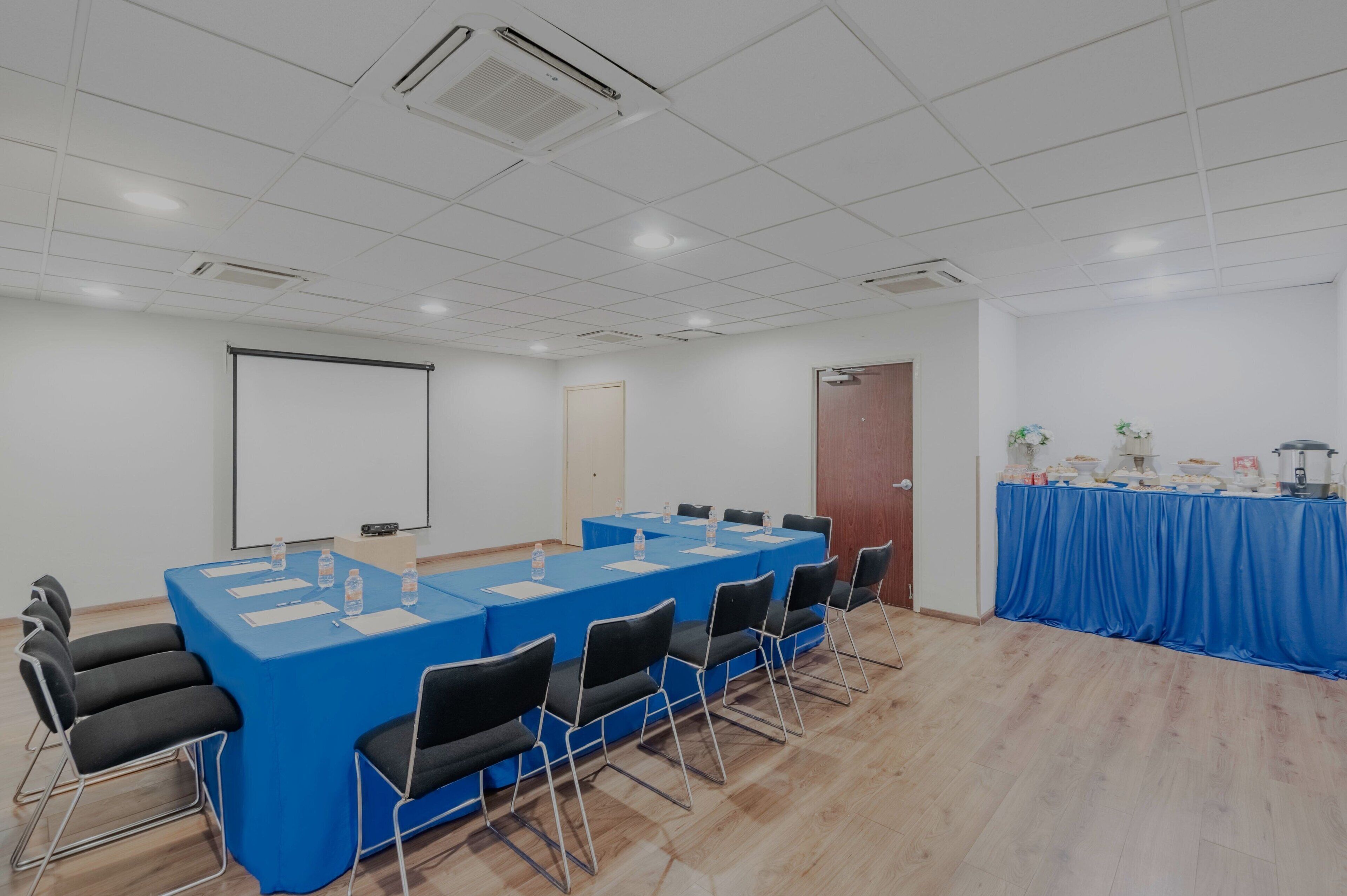 Uma sala de conferência com uma mesa comprida, cadeiras, tela de projetor e mesa de buffet.