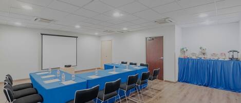 Uma sala de conferência com uma mesa comprida, cadeiras, tela de projetor e mesa de buffet.